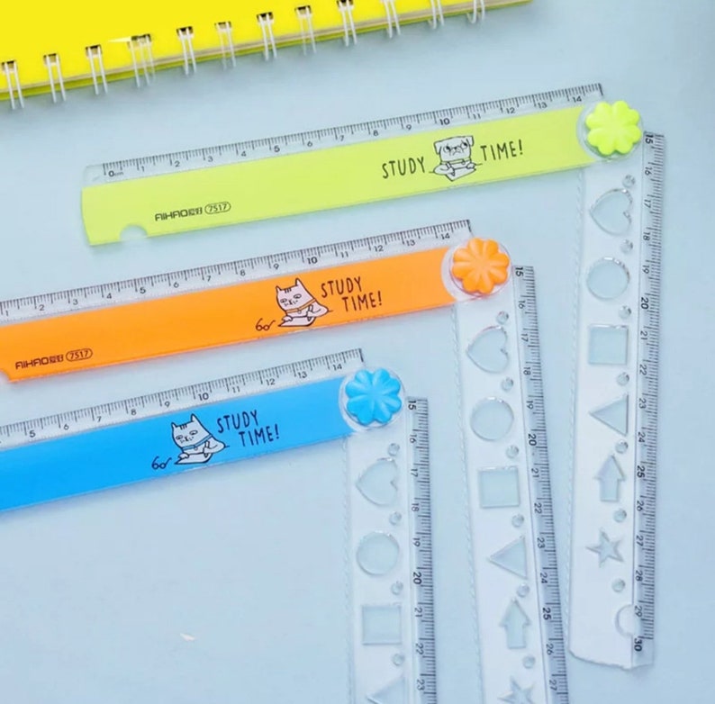 May include: Three plastic folding rulers in lime green, orange, and blue, each featuring a cartoon cat illustration and the text "STUDY TIME!". The rulers have a flower-shaped hinge and include clear sections with various geometric shape cutouts.