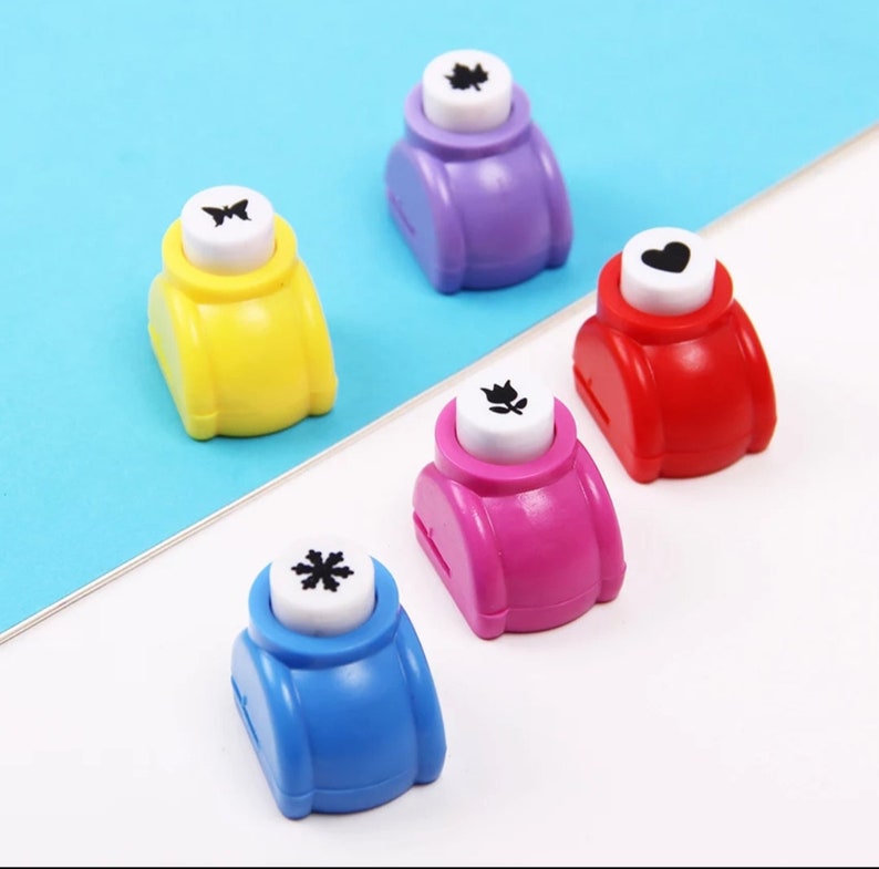 May include: Five colorful paper punchers with different designs: a butterfly, a leaf, a heart, a flower, and a snowflake. The punchers are made of plastic and have a white button with the design on it.