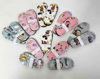 May include: A collection of 12 colorful flip flops with various cartoon characters and designs. The flip flops are pink, blue, and white with black outlines. The flip flops have numbers printed on them, ranging from 20 to 29.