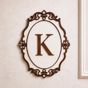 May include: A wall-mounted oval plaque featuring a dark brown wooden frame with intricate scrollwork details. The centre of the plaque is a smooth white oval surface displaying a large, dark brown wooden capital letter K in the middle.