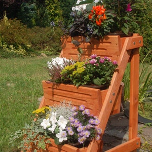 Peut inclure: Un pot de fleurs en bois à trois niveaux, chaque niveau contenant différents types de fleurs. Le pot est teinté d'une couleur brun rougeâtre et a un aspect rustique. Les fleurs comprennent des fleurs blanches, violettes, jaunes et rouges.