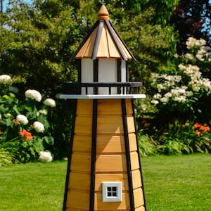 Könnte beinhalten: Ein hölzernes Leuchtfeuermodell mit einem schwarz-weiß gestreiften Design. Der Leuchtturm hat ein weißes Dach, eine weiße Tür und zwei weiße Fenster. Der Leuchtturm steht auf einem grünen Rasen.