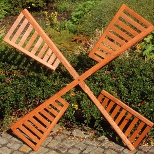 Può includere: Un mulino a vento in legno con quattro pale, ciascuna con un design a lamelle. Le pale sono dipinte di un colore marrone rossiccio e sono disposte a forma di croce.