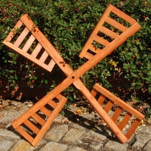 Könnte beinhalten: Eine Windmühle aus Holz mit vier Flügeln, die jeweils ein Lamellendesign aufweisen. Die Windmühle ist braun und steht auf einem Bett aus braunen Steinen.