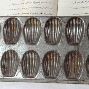 Könnte beinhalten: Eine antike Madeleinen-Backform aus Metall mit 12 einzelnen Formen. Die Form ist leicht rostig und weist Gebrauchsspuren auf.