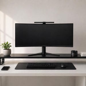Puede incluir: Una moderna configuración de oficina en casa con un monitor de computadora negro curvo, teclado y mouse sobre un escritorio blanco. Un estante negro contiene una planta en maceta, una pequeña taza negra y libros. Un teléfono inteligente y una alfombrilla de escritorio negra completan el diseño minimalista.