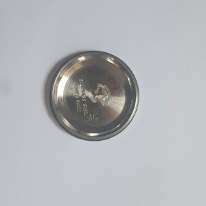 K&ouml;nnte beinhalten: Nahaufnahme eines silbernen Uhrenbodens mit der Gravur "STAINLESS STEEL" und "SWISS MADE". Der Boden hat auch ein Logo mit dem Text "11PR".