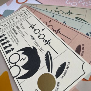 May include: A white card with a gold scratch-off area. The card has a black and white illustration of Harry Potter's glasses and a feather. The text on the card reads "Admit One", "To: Maggy", "Date: 05/07/2023", "Message: Happy Birthday Maggy! We can't wait to share this experience with you.", "From: Mammy & Daddy", "We are going to... Scratch here to find out".
