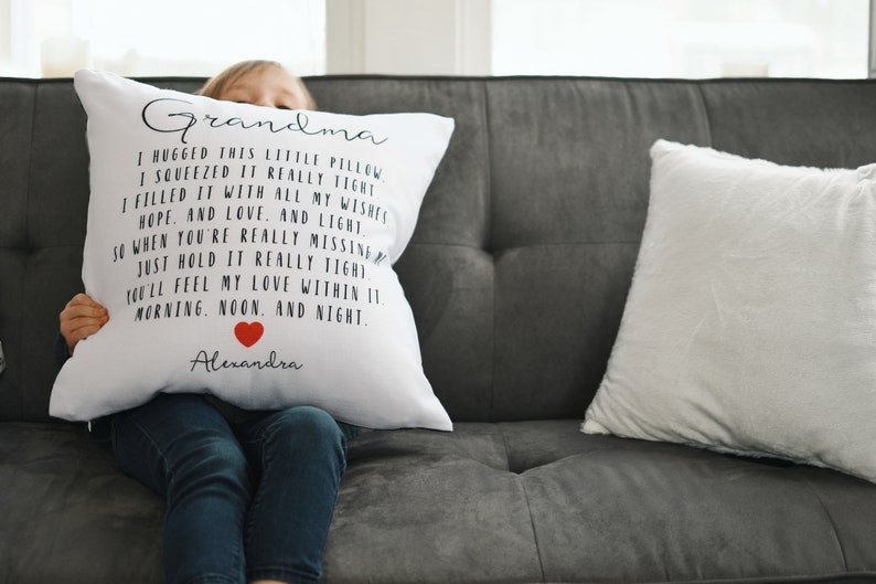 May include: White pillow with black text that reads "Grandma I hugged this little pillow I squeezed it really tight I filled it with all my wishes hope, and love, and light So when you're really missing just hold it really tight You'll feel my love within it morning, noon, and night Alexandra" with a red heart symbol.