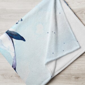 May include: A folded throw blanket with a watercolor design. The blanket features a light blue background with a dark blue and white floral design. The blanket is made of a soft, plush material.