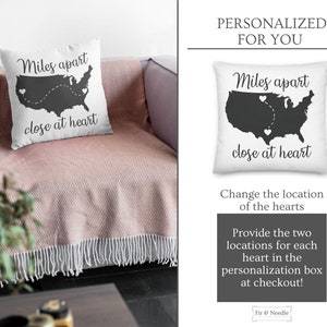 May include: White square pillow with a black silhouette of the United States, two heart icons, and the text "Miles apart close at heart." The pillow is on a pink blanket.