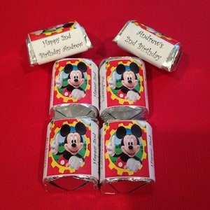 May include: Miniature candy bars with custom wrappers featuring Mickey Mouse and the text "Happy 2nd Birthday Andrew". The wrappers are red with a yellow and red gear design and a picture of Mickey Mouse.