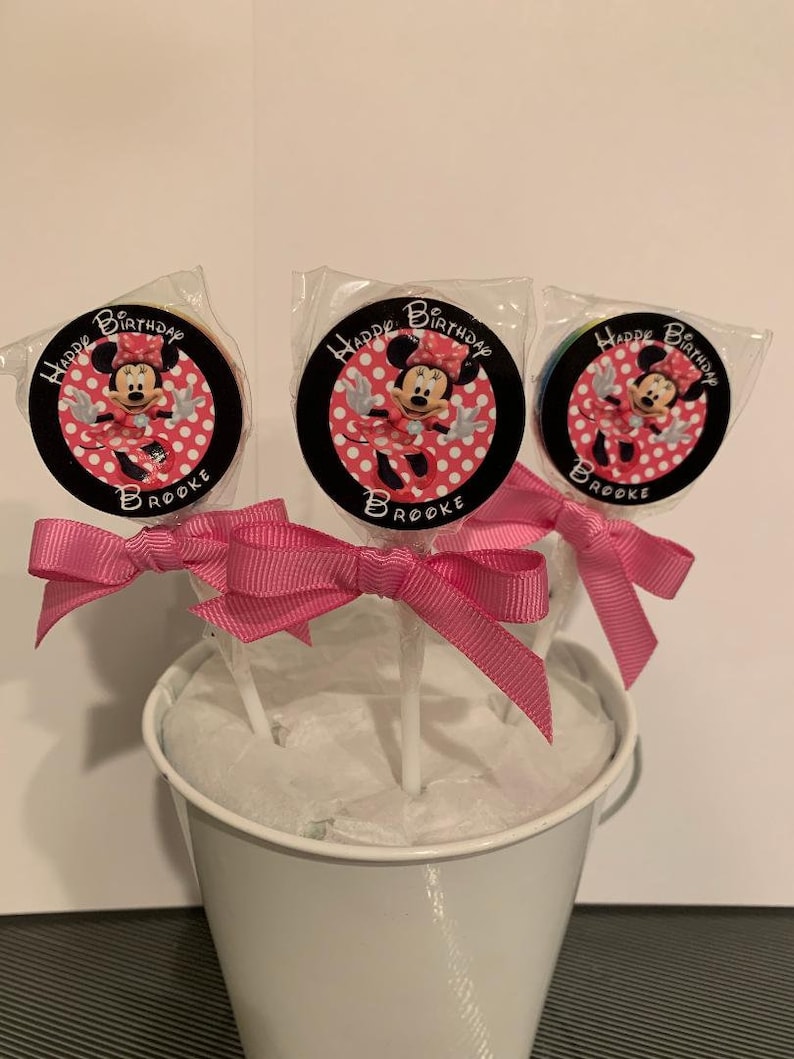 May include: Three Minnie Mouse themed lollipops with pink bows in a white bucket. The lollipops have a black background with white polka dots and the text "Happy Birthday Brooke".