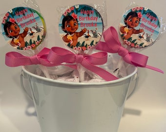 May include: Three pink and white lollipop sticks with a round, colorful, printed image of a cartoon character with the text "Happy Birthday Brooke" on each. The lollipops are in a white metal bucket.