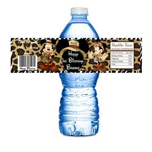 May include: Water bottle label with a jungle animal print background. The label features a cartoon image of Mickey Mouse and Minnie Mouse dressed in safari outfits. The text on the label reads "Happy 1st Birthday Brooke".