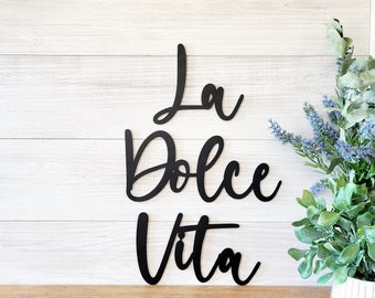 May include: Black metal wall decor with the Italian phrase "La Dolce Vita" written in a cursive font.