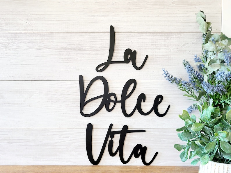 May include: Black metal wall decor with the Italian phrase "La Dolce Vita" written in a cursive font.