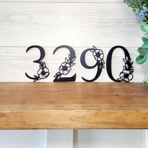 May include: Black metal house numbers with floral accents, featuring the numbers 3290. The numbers are displayed on a wooden shelf.