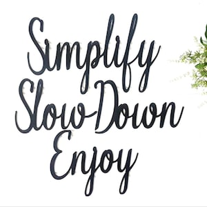May include: Black wooden sign with the words "Simplify Slow Down Enjoy" written in a cursive font.