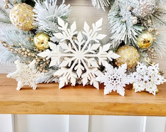 Puede incluir: Cuatro copos de nieve blancos de diferentes tamaños y diseños, dispuestos sobre una superficie de madera. Los copos de nieve están hechos de un material ligero y tienen un diseño delicado e intrincado.