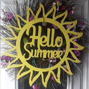 May include: A yellow wooden sun with the text "Hello Summer" on it. The sun is surrounded by a wreath of green and brown twigs, with purple flowers.