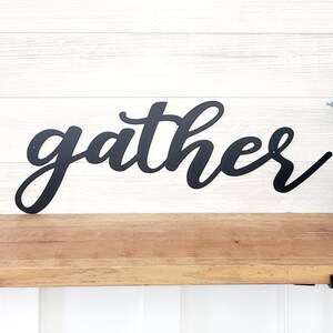 May include: Black metal wall decor with the word "gather" in a cursive font.