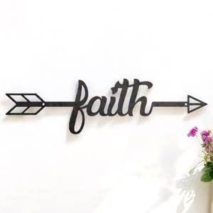 May include: Black metal wall decor featuring an arrow with the word "faith" written in a cursive font.