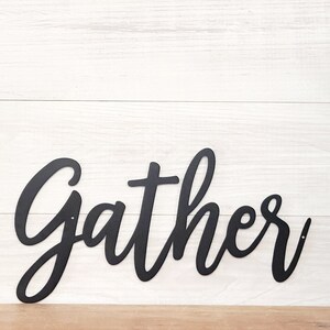 May include: Black metal wall decor with the word "gather" in a cursive font.