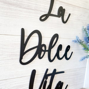 May include: Black metal wall decor with the words "La Dolce Vita" in a cursive font.