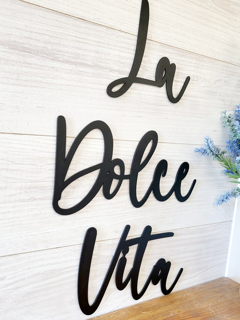 May include: Black metal wall decor with the words "La Dolce Vita" in a cursive font.