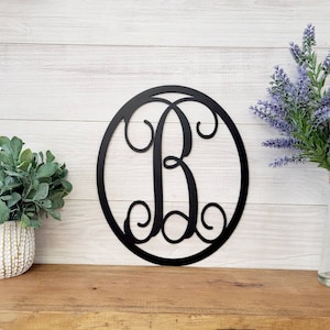 May include: Black metal monogram letter B in a circular frame. The letter is in a script font with decorative flourishes.