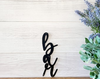 May include: Black metal wall decor with the word "bar" written in a cursive script.