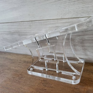 May include: A clear acrylic stand with multiple tiers for displaying items. The stand has a modern design and is made of durable acrylic.