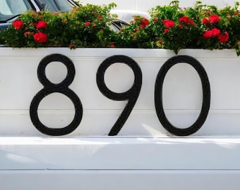May include: Black metal house numbers 890 on a white background.