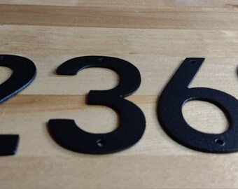 May include: Black metal house numbers 2369. The numbers are attached to a wooden surface.
