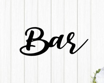 May include: Black cursive script sign that reads "Bar" on a white wood background.