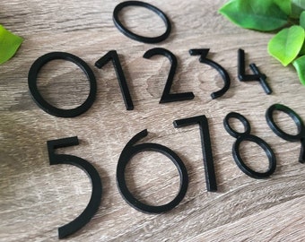 May include: Black numbers 0 through 9, with a black circle, are arranged on a wood surface. The numbers are made of a thick, black material and have a simple, modern design.