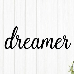 May include: Black cursive word "dreamer" on a white wood background.