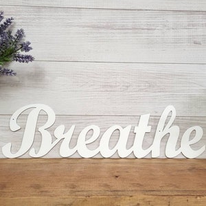 May include: White wooden sign with the word "Breathe" in a cursive font.