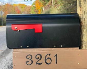 May include: A matte black metal mailbox with a bright red signal flag mounted on a light brown wooden post. The wooden post features the house number 3261 in black, decorative, serif-style metal numerals secured with small screws.