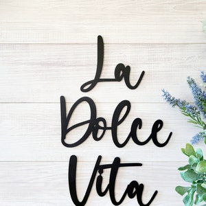 May include: Black metal wall decor with the Italian phrase "La Dolce Vita" written in a cursive font.
