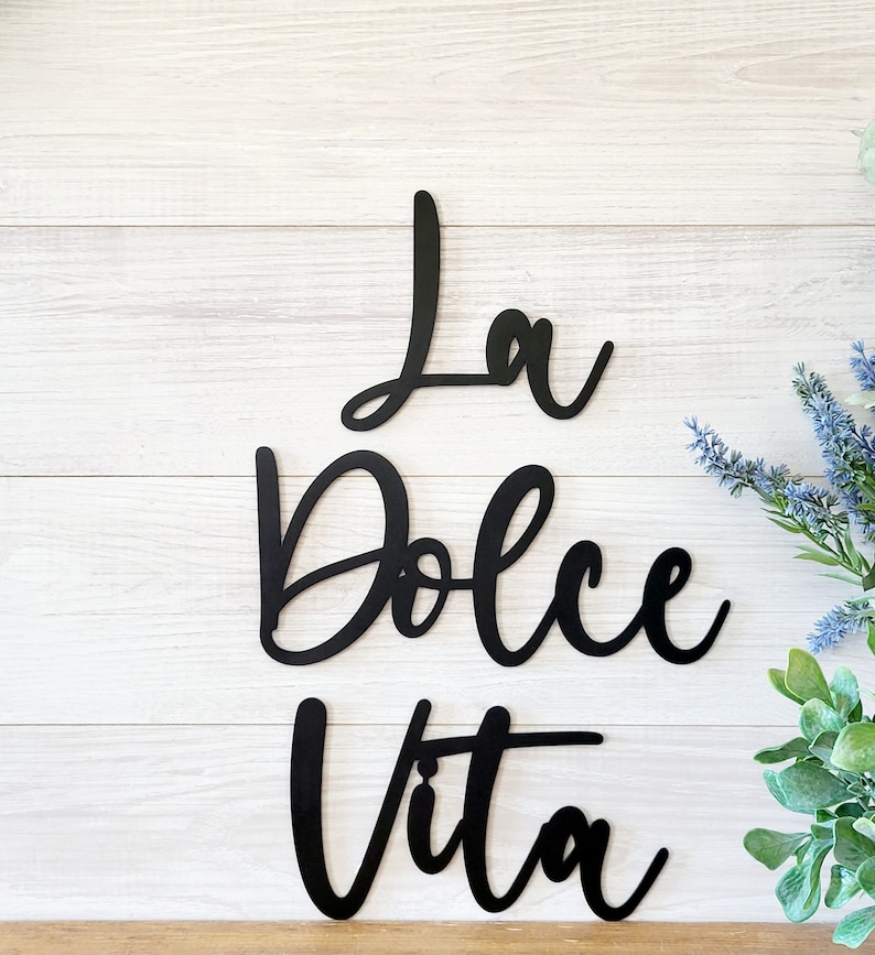May include: Black metal wall decor with the Italian phrase "La Dolce Vita" written in a cursive font.
