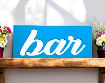 May include: A blue wooden sign with the word "bar" written in white cursive lettering. The sign is sitting on a wooden shelf.