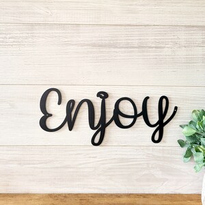 May include: Black metal wall decor with the word "Enjoy" written in a cursive font.