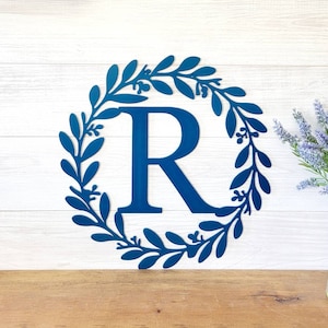 May include: A blue metal wreath with a large letter R in the center. The wreath is made of leaves and berries.