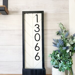 May include: Black framed wooden sign with a white chevron pattern background and black numbers 1306. The sign is sitting on a wooden surface.