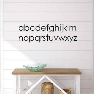 May include: White wall with the alphabet spelled out in black letters. A white table with a wooden top and a glass bowl on it. The table has two shelves with woven baskets on them.