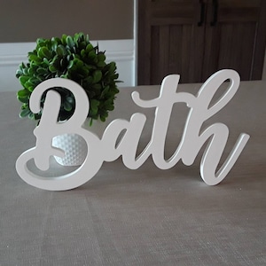 May include: White wooden sign with the word "Bath" in cursive script.