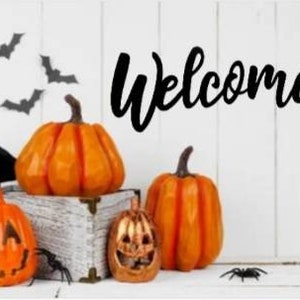 May include: A white wooden sign with the word "Welcome" in black script. The sign is decorated with orange pumpkins and black bats.