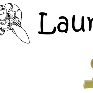 Könnte beinhalten: Eine Schwarzweiß-Zeichnung einer Schildkröte mit dem Namen "Laura" in schwarzer Kursivschrift. Ein Holz-Stempel mit runder Oberseite ist ebenfalls abgebildet.